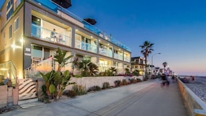 Un hôtel à plusieurs étages doté de balcons, d’une promenade dallée et de palmiers.