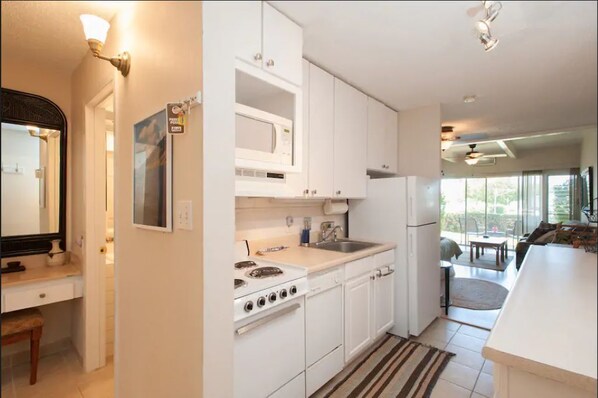 Una cocina moderna con armarios blancos, una estufa, un microondas y un refrigerador. Se ve un área de comedor a través de una puerta abierta.