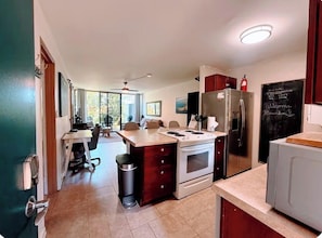 A modern kitchen with a central island, a refrigerator, and a chalkboard with writing. -  Steps to the Beach + 5-Min Walk to bites and bars (Kihei)
