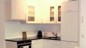 A compact kitchen with white cabinets, a black countertop, a built-in oven, a coffee maker, and a sink. - Les Dauphinelles by Interhome (Thyon-Les Collons)