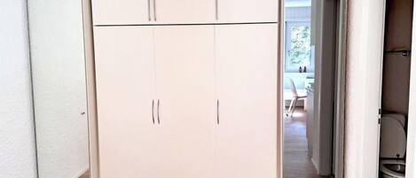 Une pièce dotée d’une grande armoire, d’un plancher en bois et donnant sur un coin repas par une porte ouverte.