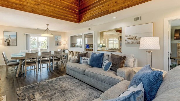 A spacious living area with a wooden ceiling, a grey sofa set, a dining table with chairs, and a large rug. - Saltwater Charm | 995 ft. to the Beach | Private Pool (Virginia Beach)