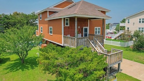 A two-story wooden house with a balcony and a small deck, surrounded by greenery. - Saltwater Charm | 995 ft. to the Beach | Private Pool (Virginia Beach)