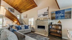 A living room with a fireplace, a sofa, a bookshelf, and a painting on the wall. - Saltwater Charm | 995 ft. to the Beach | Private Pool (Virginia Beach)