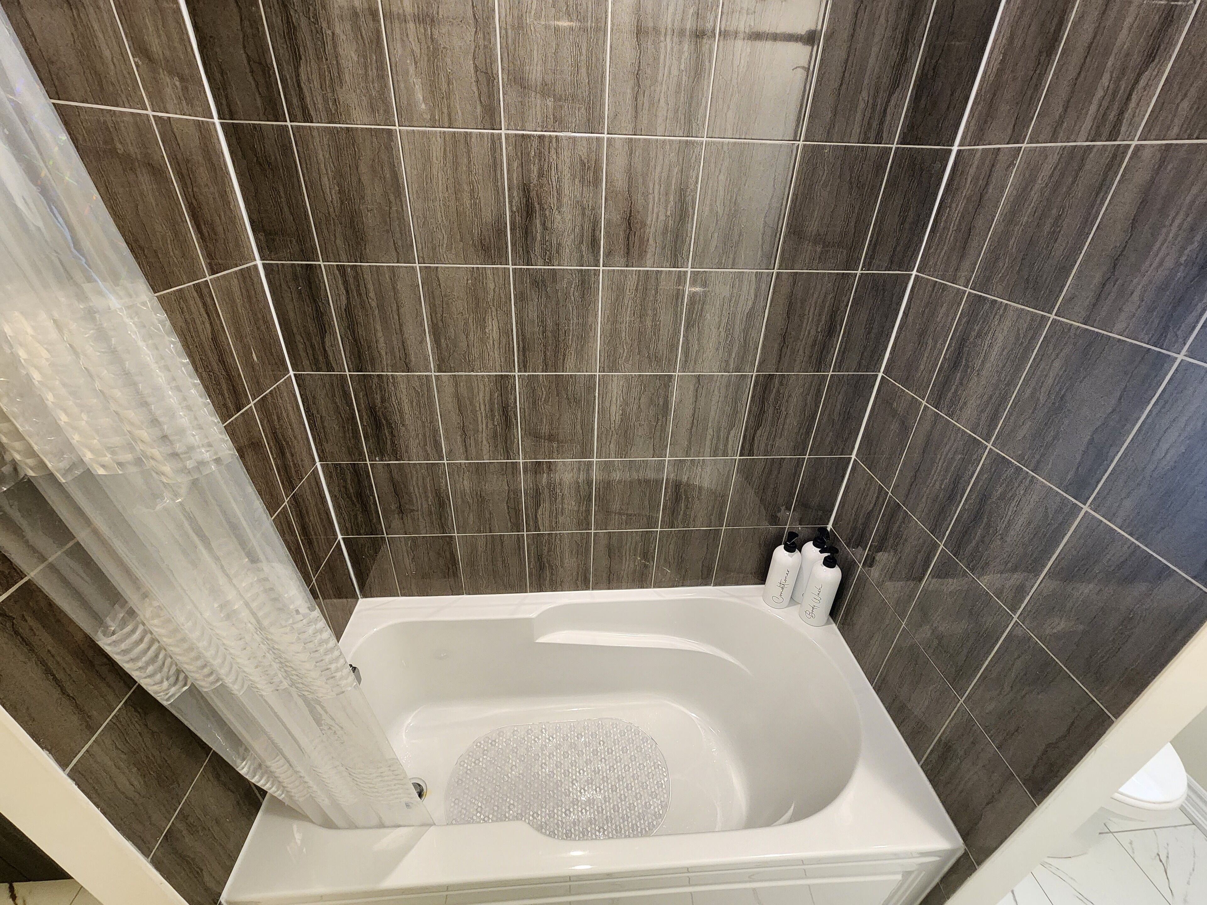 A modern bathroom with a freestanding bathtub, dark tiled walls, and a shower curtain.