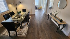 A dining area with a glass table, black chairs, and a floor lamp. There is a hallway leading to another room. - Cozy Niagara Retreat ,15 min drive to Niagara Falls, 4 bdrms, sleeps up to 9 (Thorold)