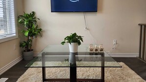 A living room with a glass coffee table, a potted plant, and a flat-screen TV displaying the Prime Video logo. - Cozy Niagara Retreat ,15 min drive to Niagara Falls, 4 bdrms, sleeps up to 9 (Thorold)