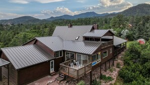 A cabin with a metal roof, large windows, and a deck overlooking a forested mountain area. - 4BR 4BA multi-family with multiple outdoor & indoor living spaces, hot tub, BBQ. (Colorado Springs)