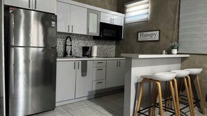 Una cocina moderna con electrodomésticos de acero inoxidable, armarios blancos, salpicadero de azulejos y una zona de bar con taburetes.