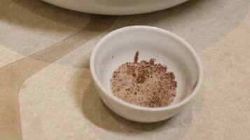 A bowl with a black rim and a small bowl of brown powder on a tiled surface.