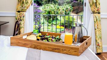 Bandeja de desayuno con ensalada, pan y jugo de naranja sobre una cama, con vistas a un jardín a través de una ventana.