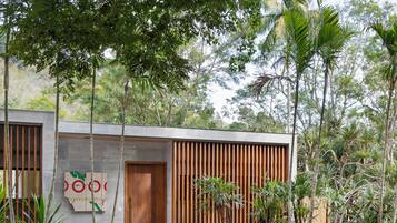 Un edificio moderno con puerta de madera y fachada de concreto, rodeado de follaje tropical.