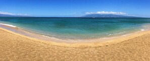 A beach with clear turquoise water, a sandy shore, and distant mountains.