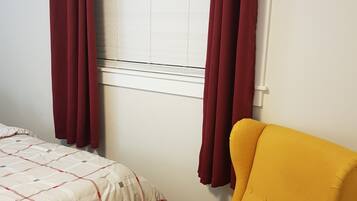 Una habitación con una cama, un sillón amarillo y un ventanal con cortinas.