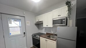 A compact kitchen with white cabinets, a microwave, a stove, and a refrigerator. - East End Suite (Eastern Passage)