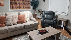 A living room with a sofa, a coffee table, a leather chair, a small table with a keyboard, and a potted plant. - East End Suite (Eastern Passage)