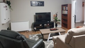 A living room with a TV, a bookshelf, a coffee table, and a sofa. - East End Suite (Eastern Passage)