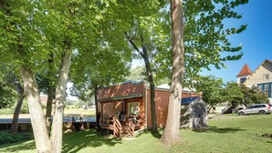 Eine kleine Holzhütte mit Veranda, umgeben von Bäumen, mit einem Haus im Hintergrund.