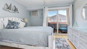 A bedroom with a bed, a dresser, a window with curtains, and a view of the outside balcony.