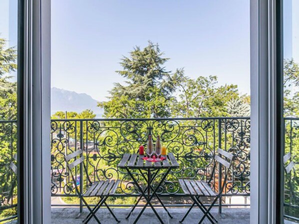 A balcony with a table and chairs, a view of trees and mountains, and a clear sky. - Le Jazz by Interhome (Montreux)