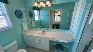 A bathroom with a white sink, a toilet, and a mirror. There are two wall clocks and a window with blinds. - Heart of Ocean Drive just one block to the Beach and Main Street  (North Myrtle Beach)