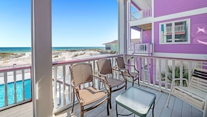 A balcony with wicker chairs and a table overlooking a beach and a swimming pool. - Holiday Summer Sale! Sundancer E/W. 10BR. Sleeps 36. Beachfront. Pool! PERFECT location. 😎 (Gulf Shores)