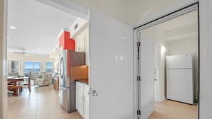 A modern kitchen with white cabinets, a stainless steel refrigerator, and a dining area with a table and chairs. - Holiday Summer Sale! Sundancer E/W. 10BR. Sleeps 36. Beachfront. Pool! PERFECT location. 😎 (Gulf Shores)