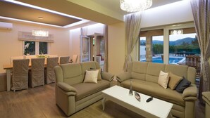 Een moderne woonkamer met een zithoek, een eethoek en uitzicht op een zwembad en bergen.