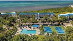 Un complexe hôtelier comprenant plusieurs bâtiments, une piscine, des courts de tennis et offrant une vue sur l’océan.