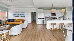 A modern kitchen with white cabinets, a stainless steel refrigerator, and a central island with bar stools. - Steps to Sand + Gulf Views, 2 Kings, Firepit, Dog Friendly (Crystal Beach)