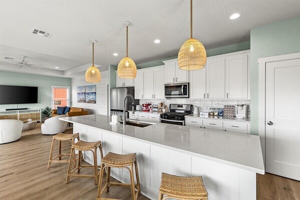 A modern kitchen with white cabinets, a large island with bar stools, and pendant lighting.