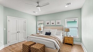 A bedroom with a bed, two nightstands, a ceiling fan, and a large window with blinds. - Steps to Sand + Gulf Views, 2 Kings, Firepit, Dog Friendly (Crystal Beach)