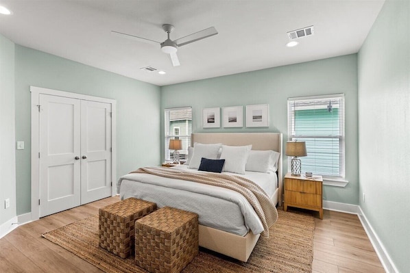 A bedroom with a bed, two nightstands, a ceiling fan, and a large window with blinds.