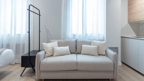 Un saló modern amb un sofà, una làmpada de peu i una cuina amb un rentaplat i armaris.