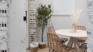 Zona de menjador amb taula rodona, cadires de vimetla, una planta en test i una paret blanca amb textura.
