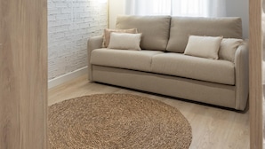 A living room with a beige sofa, a woven rug, and a white brick wall. - Meraki Suites (2 Rooms) (Astorga)