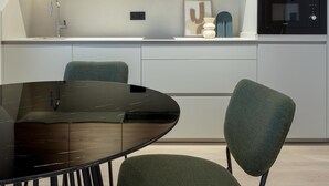A modern kitchen with a black dining table, two green chairs, and a built-in oven. - Meraki Suites (2 Rooms) (Astorga)
