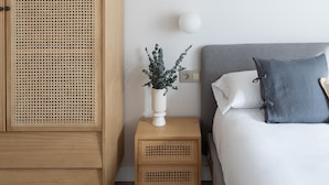 A bedroom with a wooden wardrobe, a bedside table with a vase of greenery, a grey headboard, and a grey pillow. - Meraki Suites (2 Rooms) (Astorga)