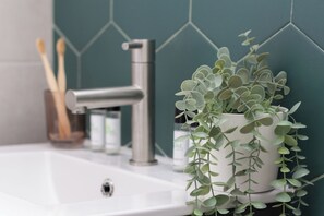 A bathroom sink with a modern faucet, a potted plant, and a toothbrush holder with toothbrushes. - VLC HOST - J.J Sister (Valencia)