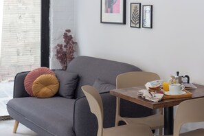 A modern living room with a grey sofa, beige chairs, a wooden table with breakfast items, and framed artwork on the wall. - VLC HOST - J.J Sister (Valencia)