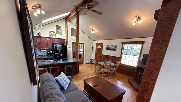 A spacious living area with a gray sofa, wooden coffee table, and a dining table with chairs. A kitchen with wooden cabinets and a refrigerator is visible in the background. - Wonderfully located near Bay Street and all the wonderful restaurants. Sauna! (Florence)