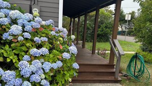 A covered porch with steps leading to a house, surrounded by lush greenery and hydrangea bushes. - Wonderfully located near Bay Street and all the wonderful restaurants. Sauna! (Florence)