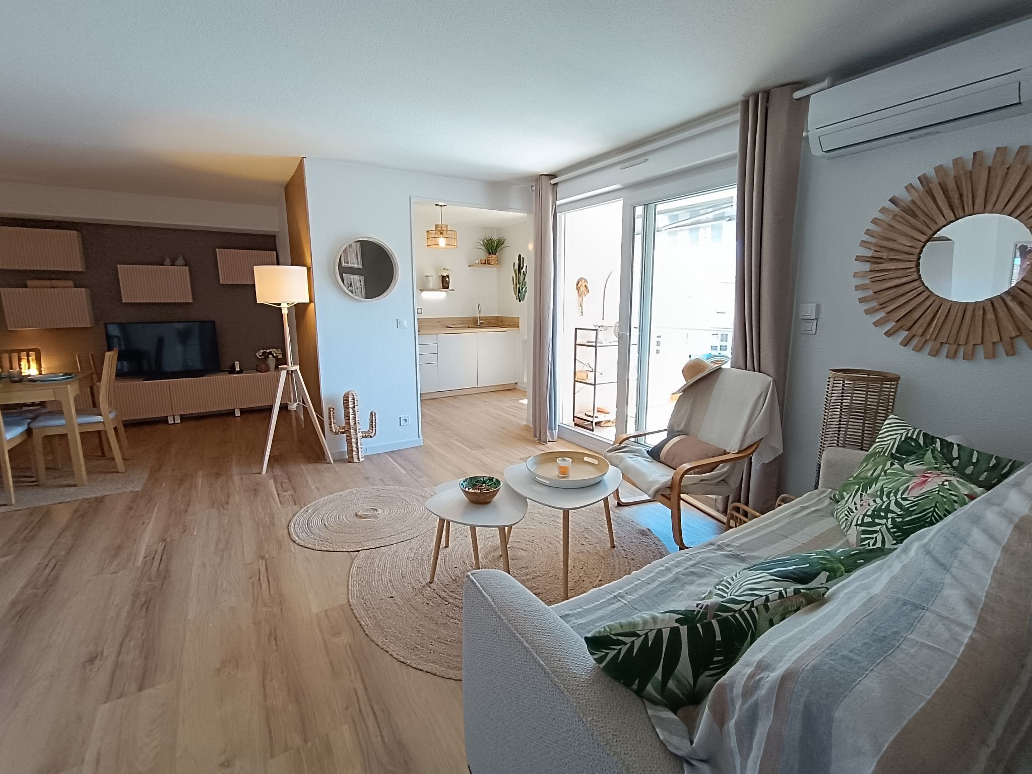 A modern living room with a sofa, coffee table, and dining area. There is a kitchen in the background with a large window.