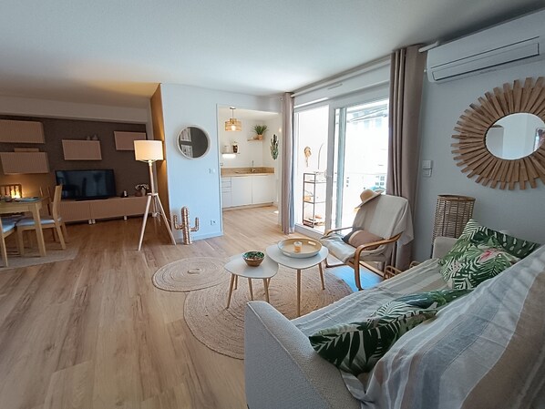 A modern living room with a sofa, coffee table, and dining area. There is a kitchen in the background with a large window.