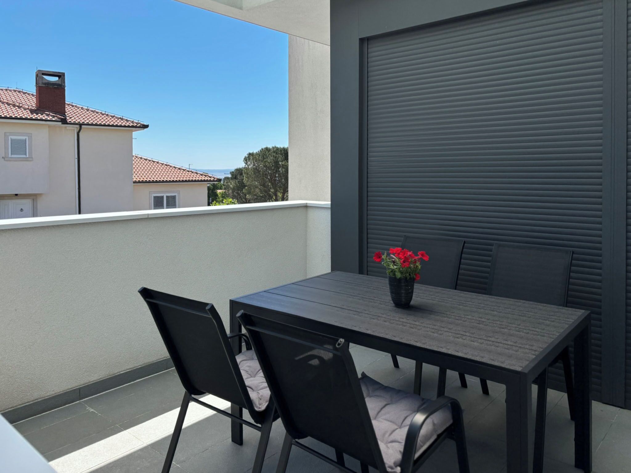 Een balkon met een tafel, stoelen, een bloempot en een gesloten rolluik.