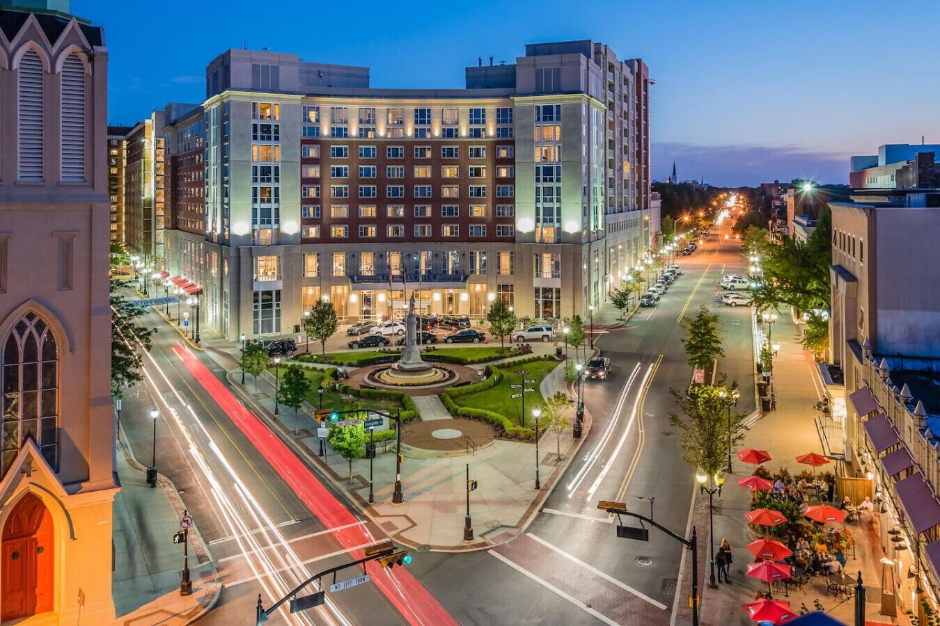 A multi-story hotel with a central courtyard, a roundabout, and a street with cars and pedestrians.