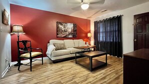 Una sala de estar con una pared roja, un sofá blanco, una mesa de centro de madera, una lámpara y un ventilador de techo.