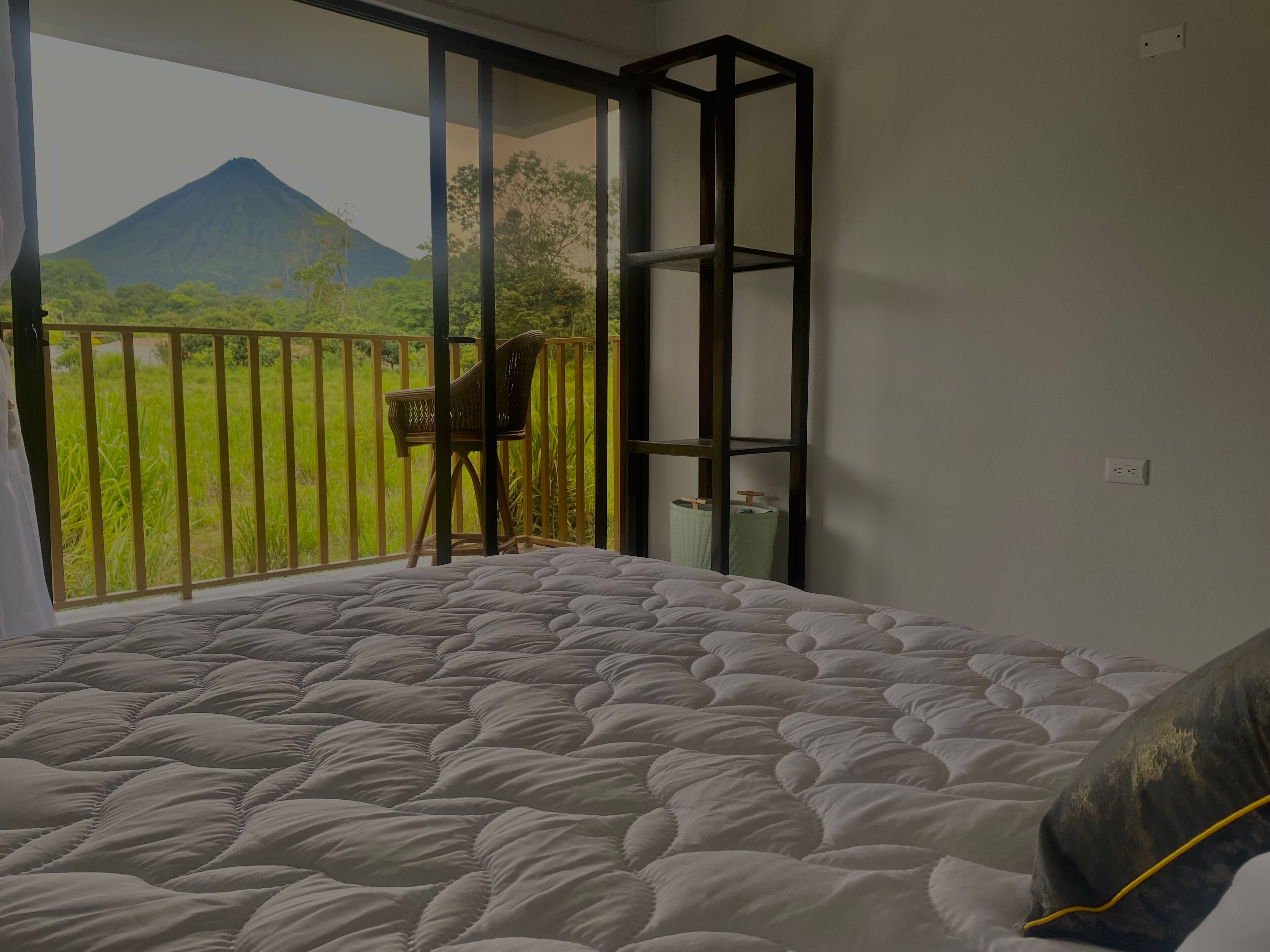 A bedroom with a bed, a chair, a balcony with a view of a mountain, and a shelf.