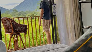 A room with a bed, a wicker chair, and a view of a mountain.