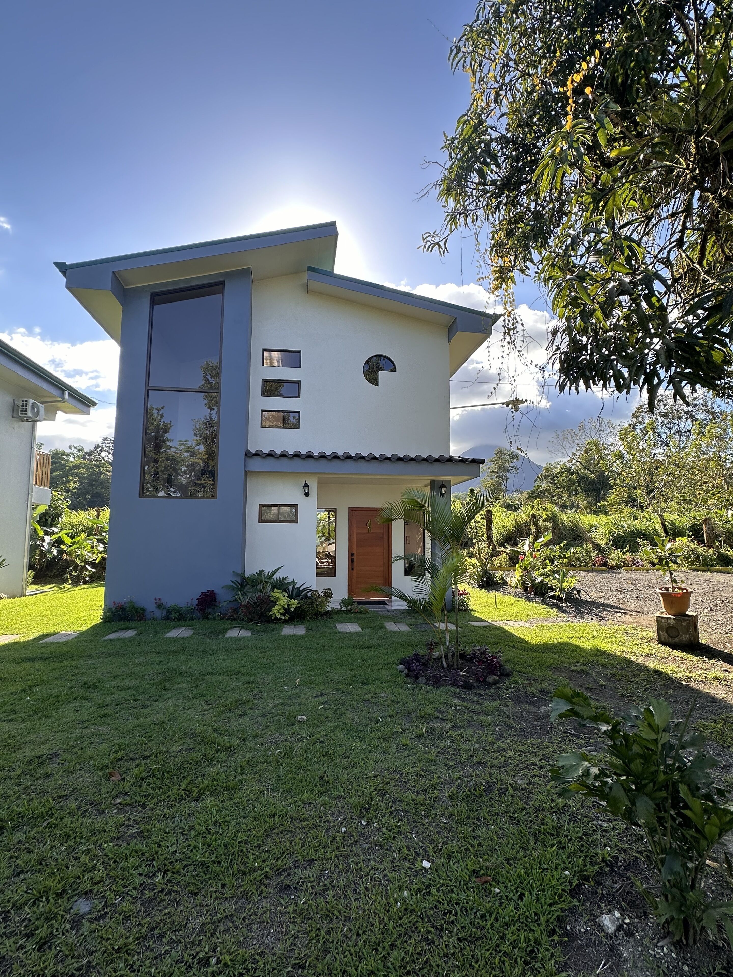 A modern two-story house with a flat roof, a large window on the upper floor, and a small front porch.